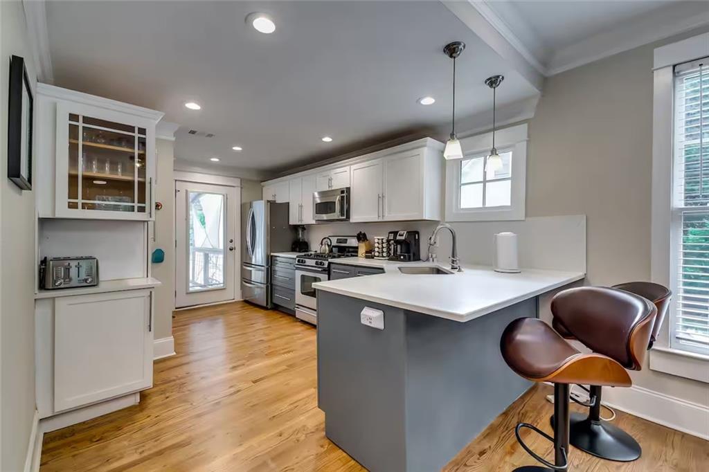 Kitchen with a large gray island, white cabinets, stainless steel appliances, and hardwood floors.