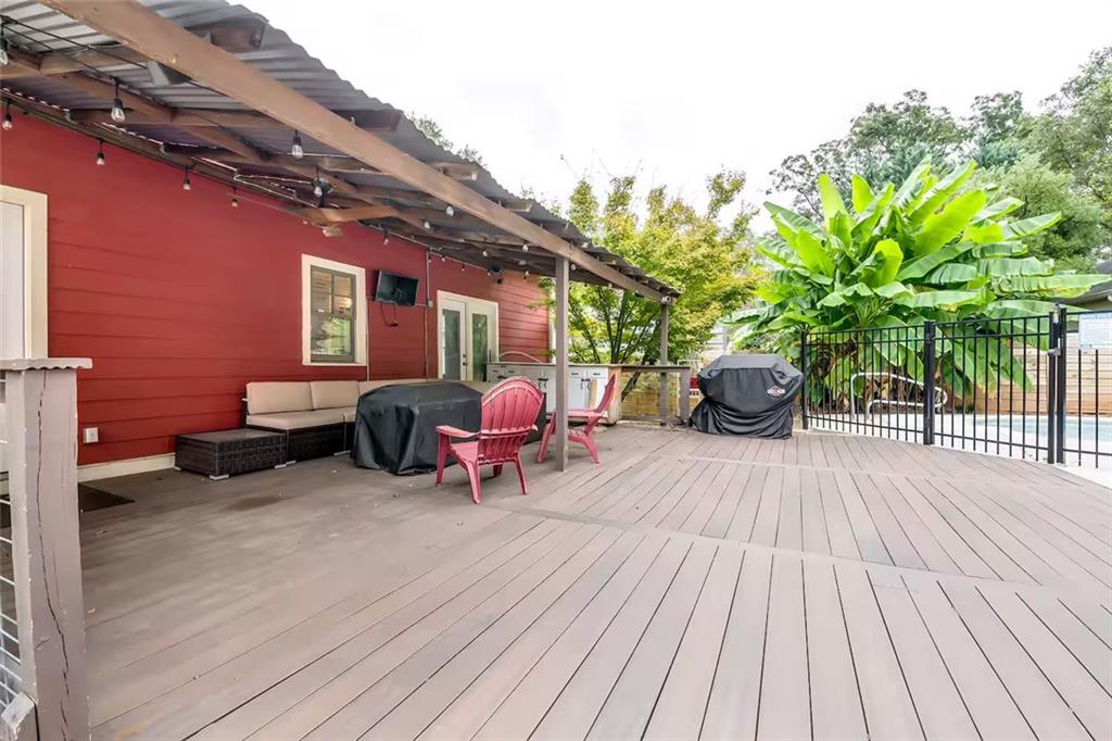 Raised deck beside a red house with outdoor seating, covered grills, and leafy plants.