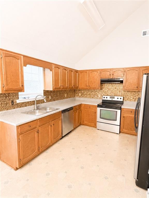 Kitchen with honey-colored cabinets, speckled counters, a window-side sink, and stainless steel appliances.