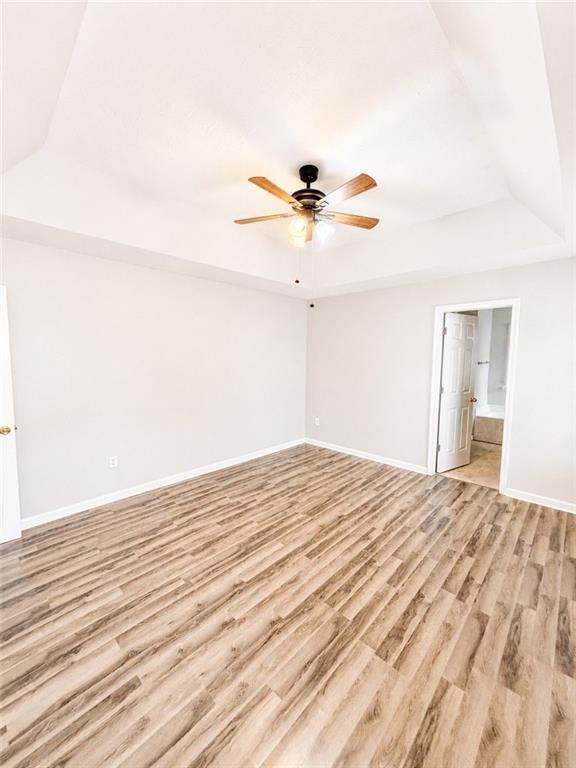 Empty bedroom with wood-look flooring, a tray ceiling, and an open doorway to a bathroom.