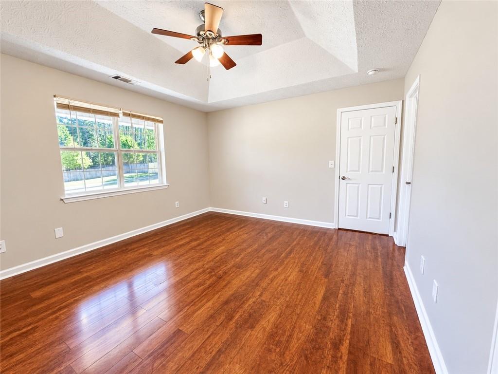 Empty room with polished hardwood floors, a large window, and a vaulted ceiling with a ceiling fan.