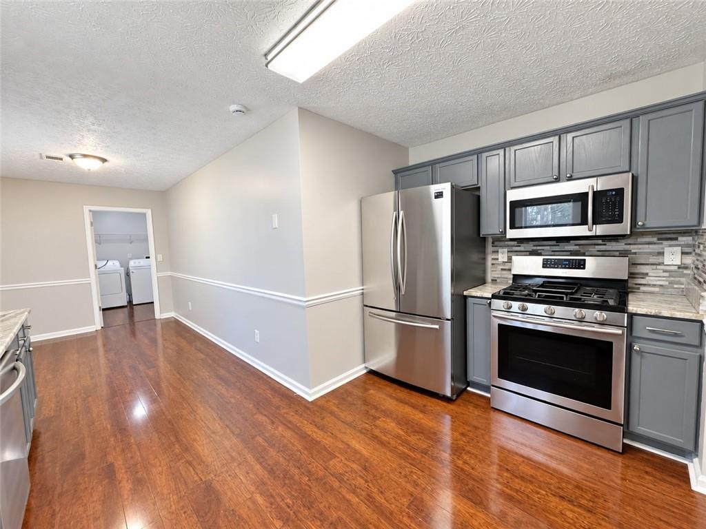 Kitchen with gray cabinets and stainless steel appliances, with a laundry area visible through the doorway.