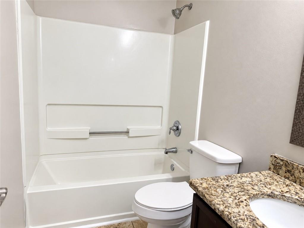 Bathroom with a white tub and shower, toilet, and granite vanity.