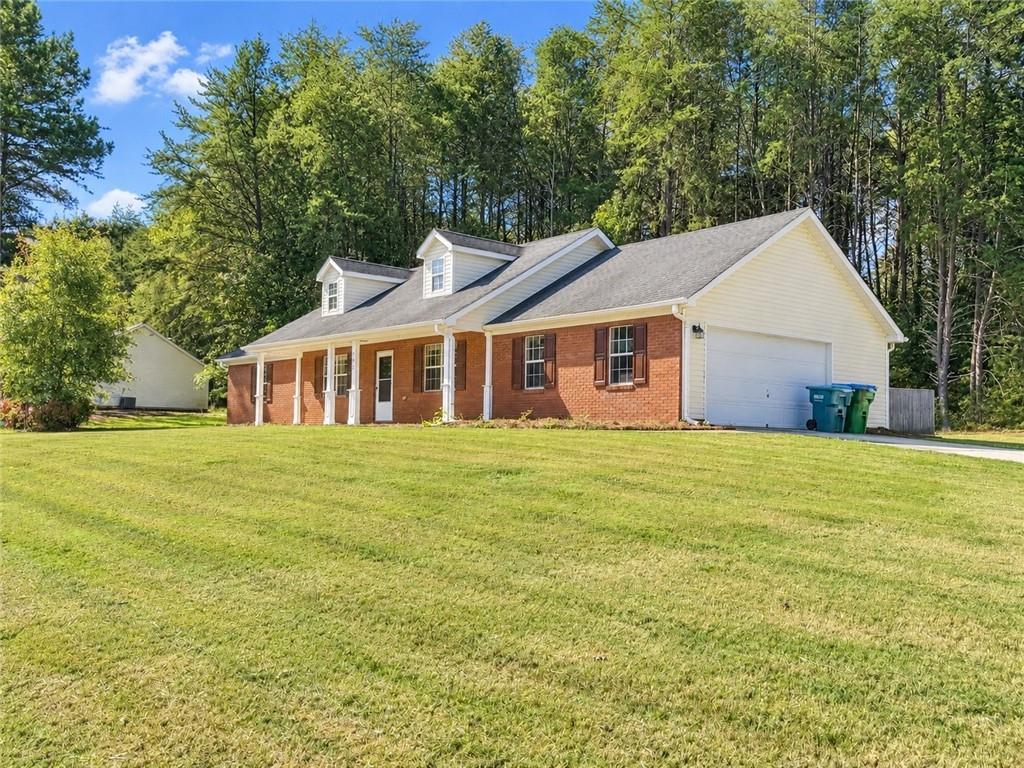 Brick ranch home with white garage, roof dormers, broad lawn, and wooded backdrop.