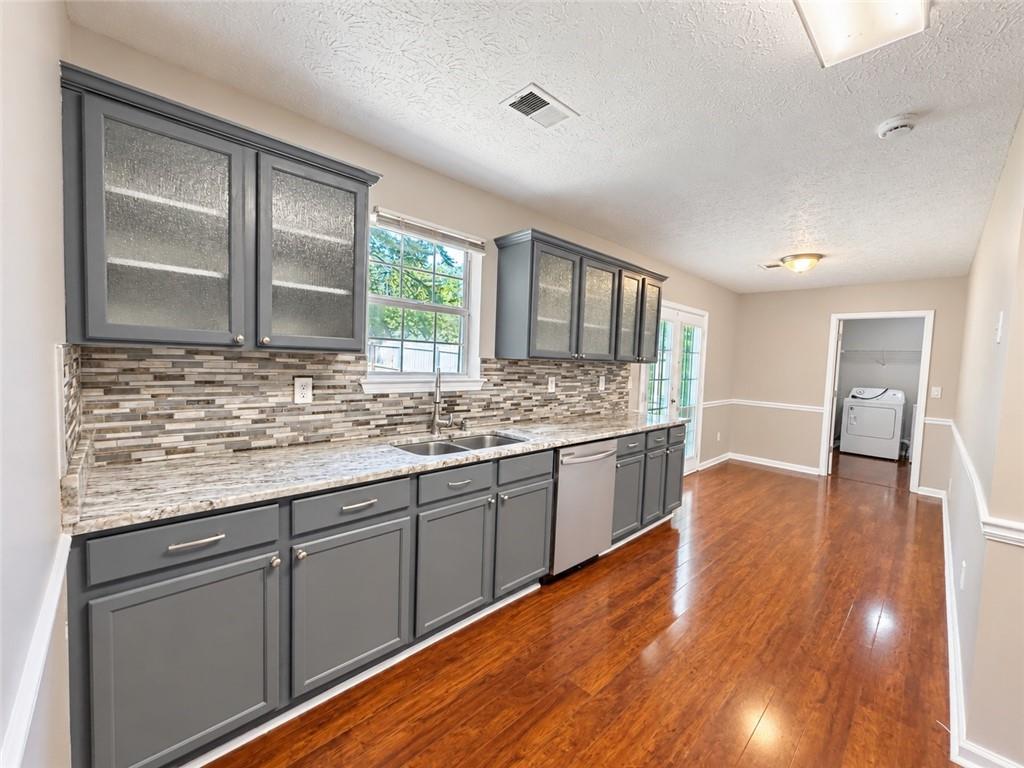 Kitchen with gray cabinets, granite counters, and hardwood floors; laundry area visible at the far end.