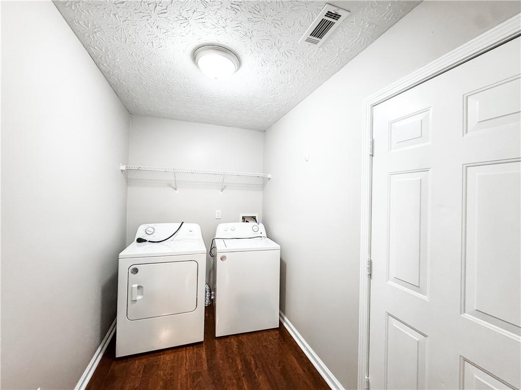 Laundry room with white washer and dryer, wire shelf, and dark wood-look floor.