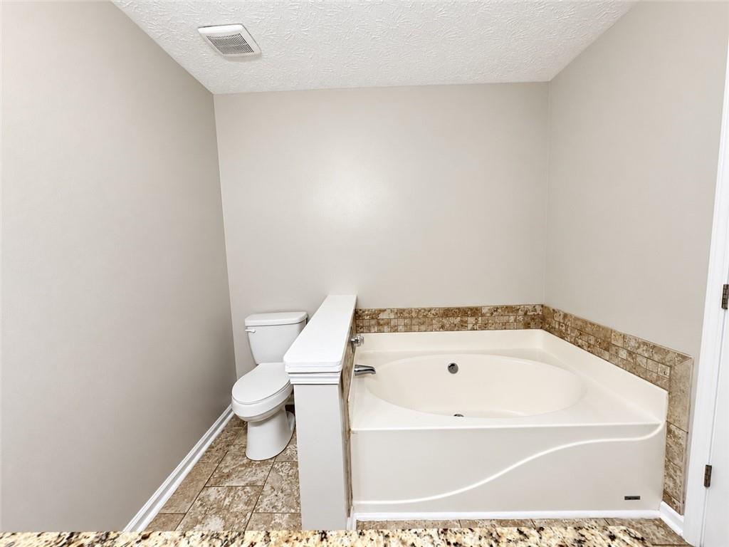 Bathroom with a large corner jetted tub and beige tile surround beside a toilet.