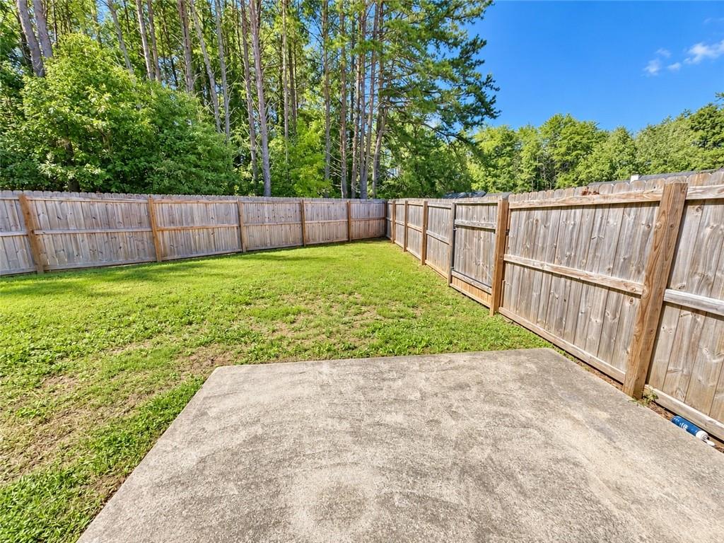 Fenced backyard with a concrete patio, lawn, and mature trees behind a wooden privacy fence.