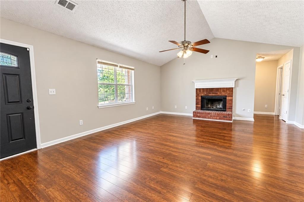 Vacant living room with glossy wood floors, a brick fireplace, and a vaulted ceiling.