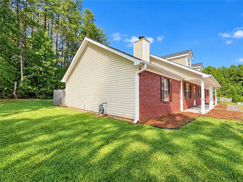 House with red brick and light siding, covered porch, and green lawn bordered by trees.