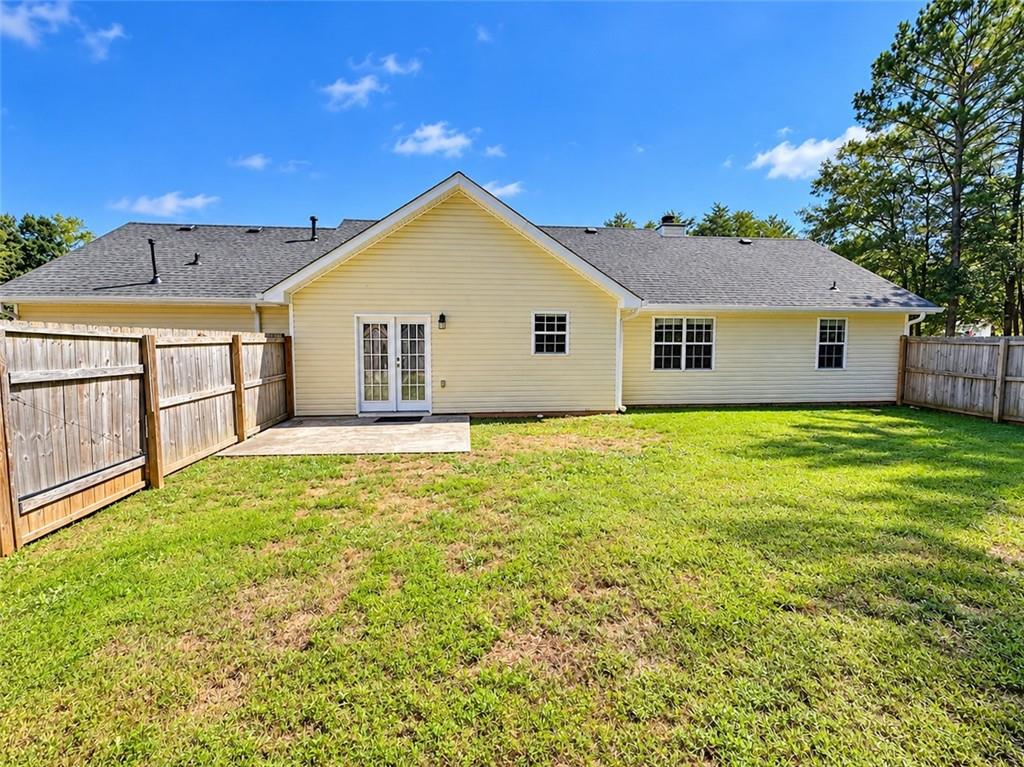 Rear of a yellow-sided home with a small patio and fenced grassy backyard.