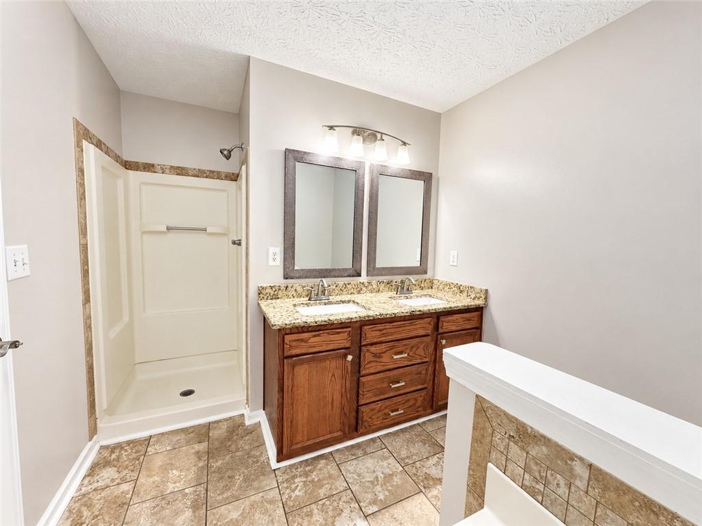 Bathroom with a walk-in shower and double-sink wood vanity topped with granite.