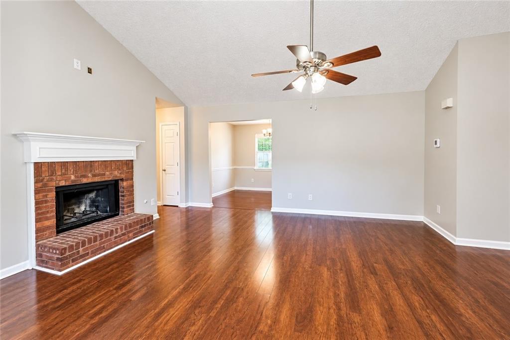 Empty living room with a brick fireplace, hardwood floors, and a ceiling fan.