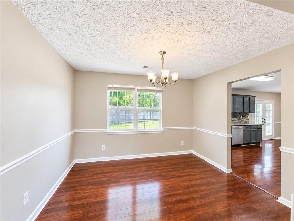 Empty dining room with hardwood floors, a chandelier, and a window overlooking the fenced yard.