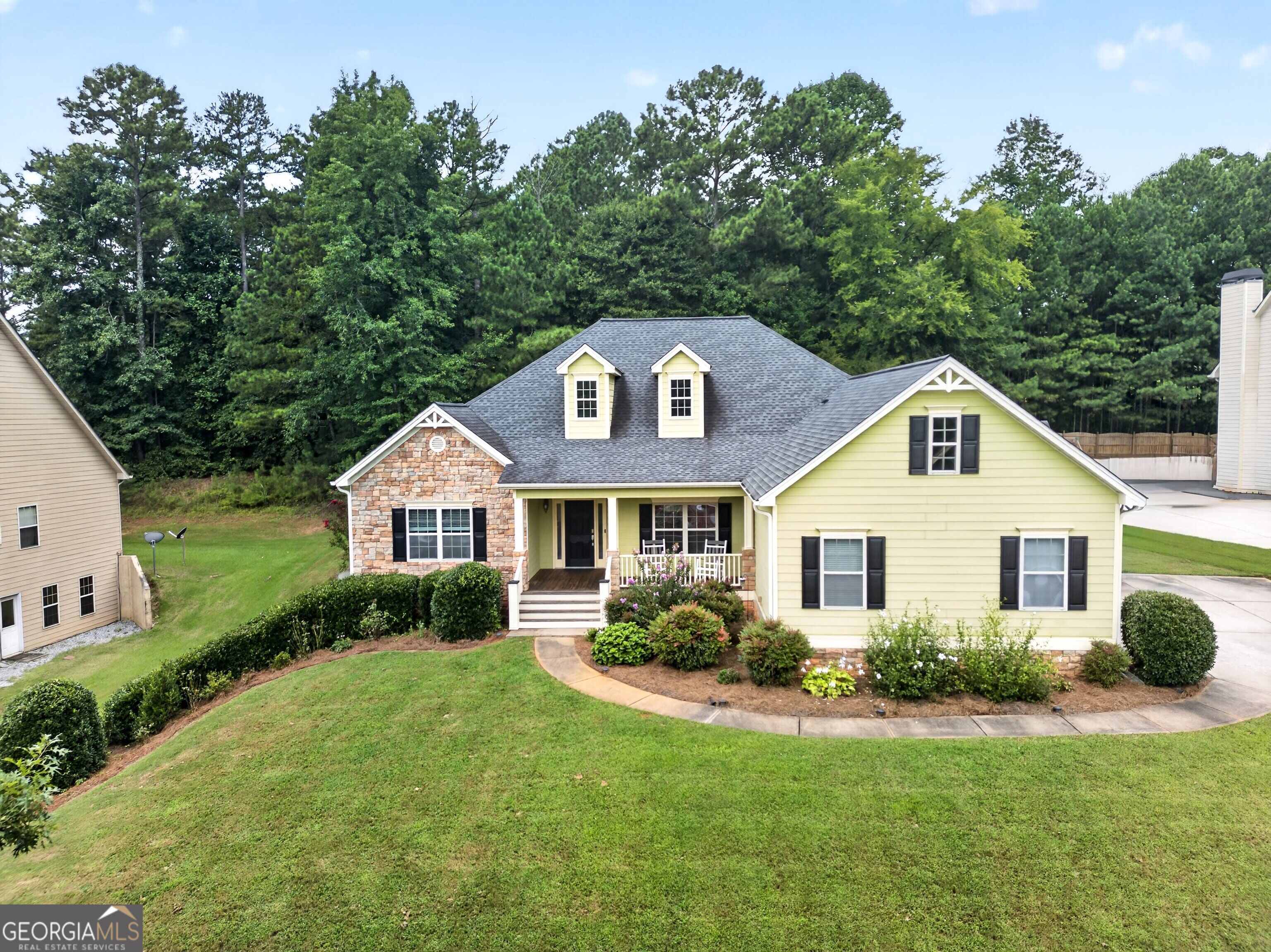 Pale yellow house with a stone facade, covered porch, dormers, and landscaped front lawn.