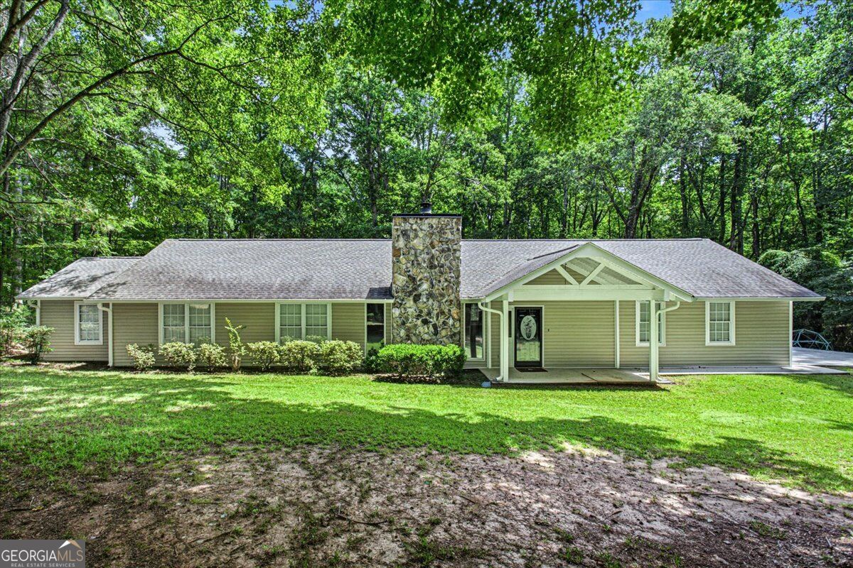 Ranch-style home with a stone chimney and covered porch in a leafy wooded setting.