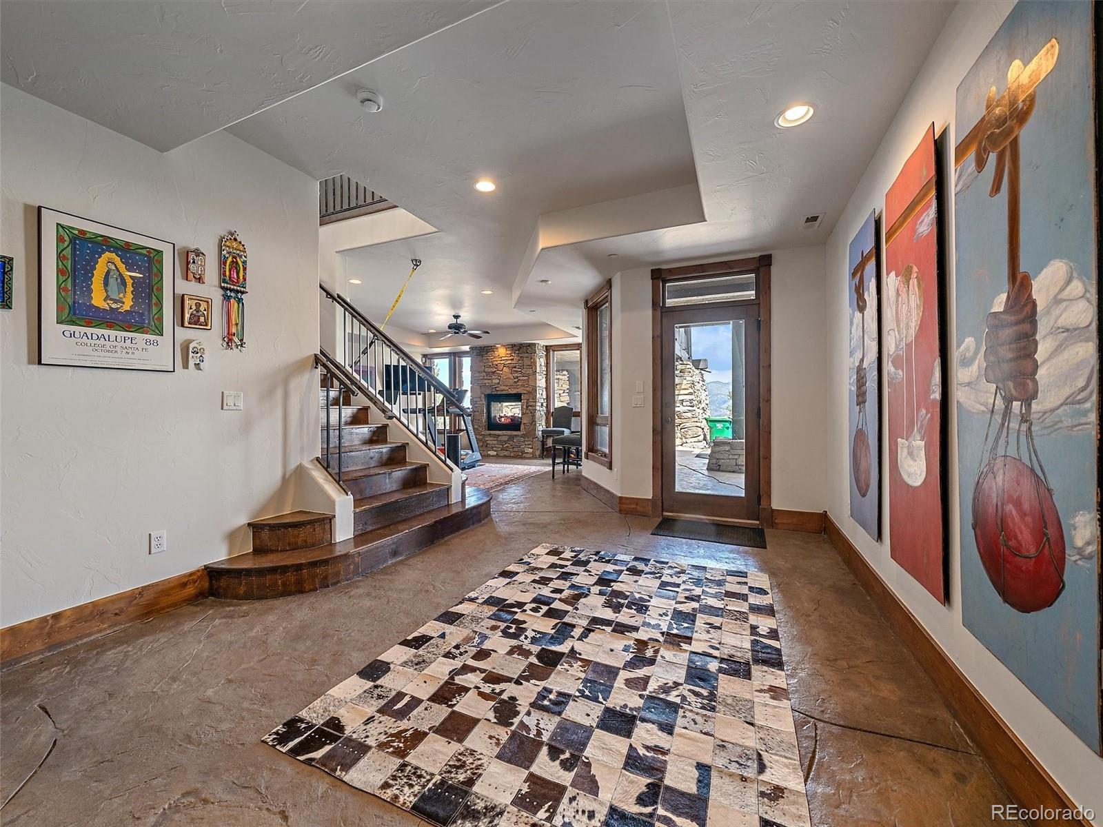 Entry foyer with a dark wood staircase, stone fireplace, and colorful artwork along the wall.