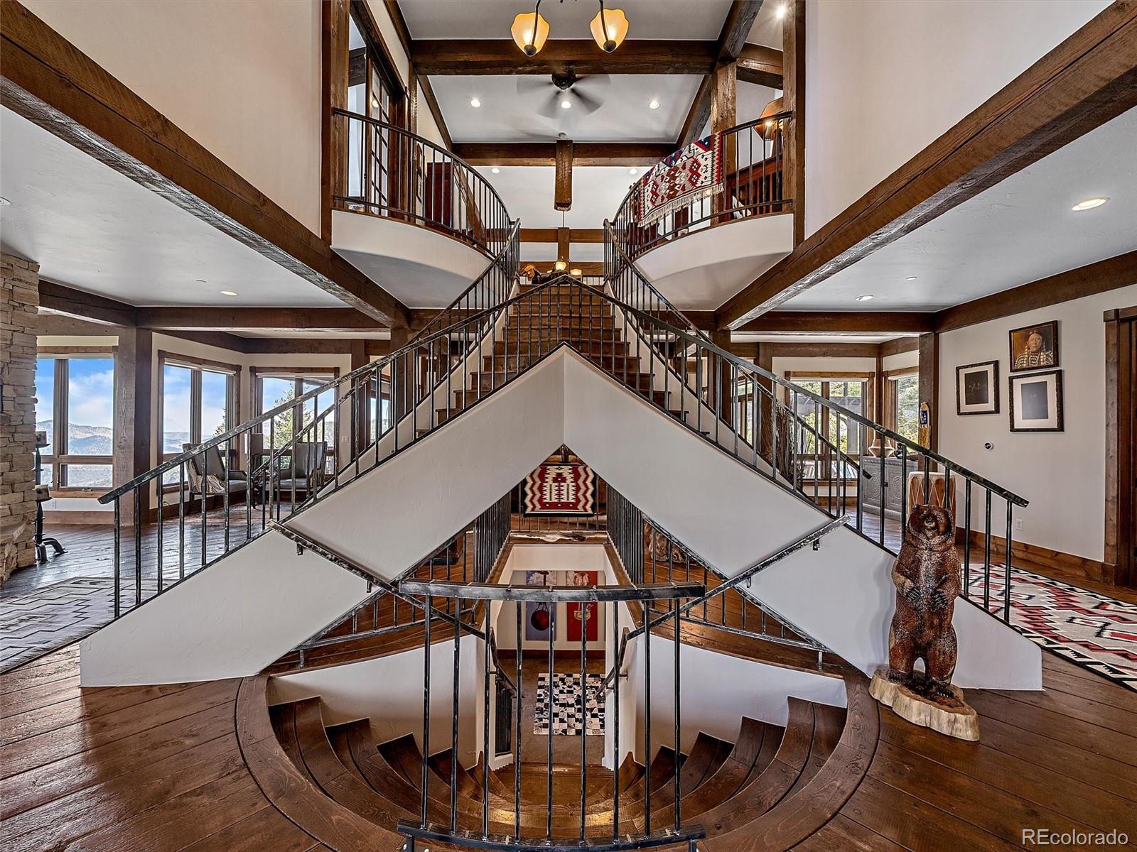 Multi-level staircase with curved wooden steps, timber beams, black railings, and mountain-view windows.