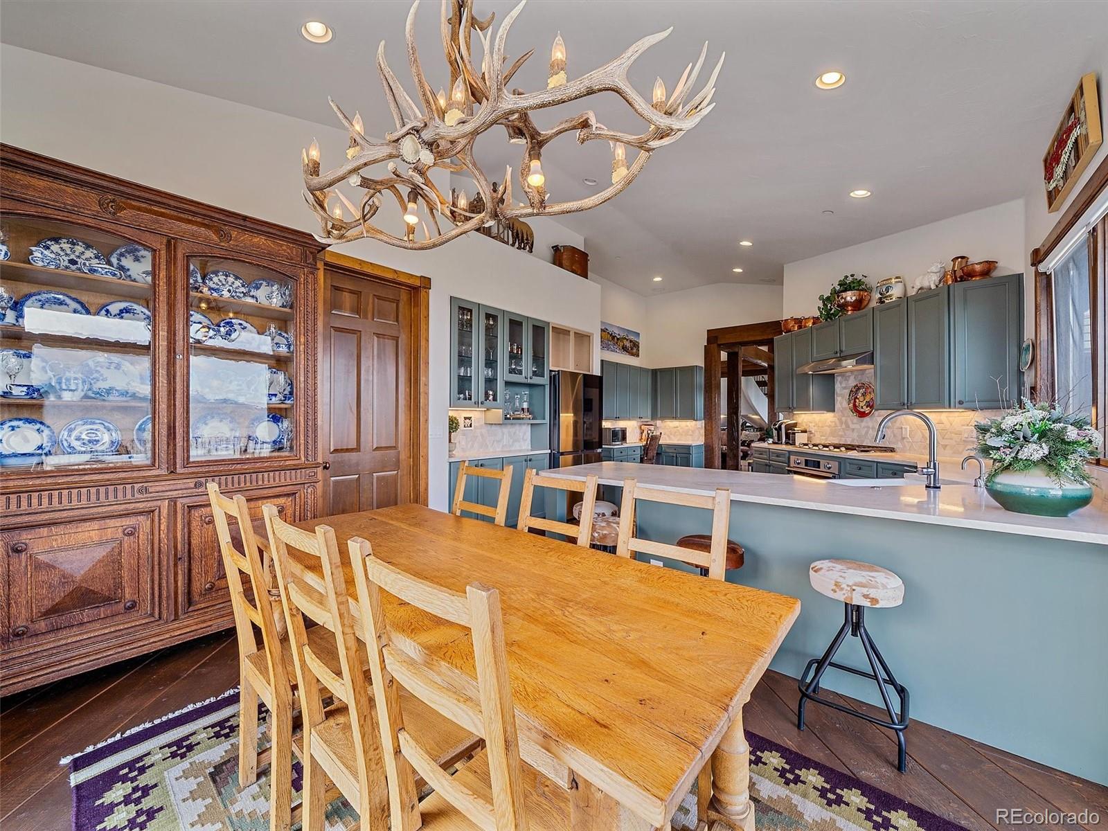 Kitchen and dining area with blue-gray cabinets, a long island, antique china cabinet, and antler chandelier.