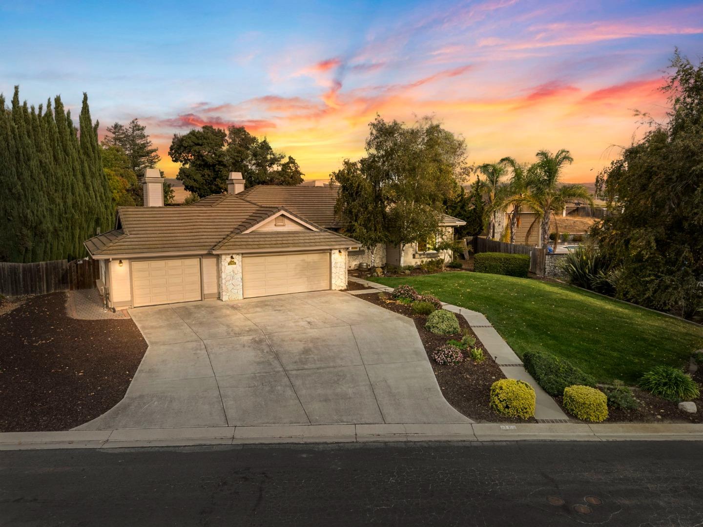 Single-story home with a tile roof, broad driveway, and landscaped yard at sunset.