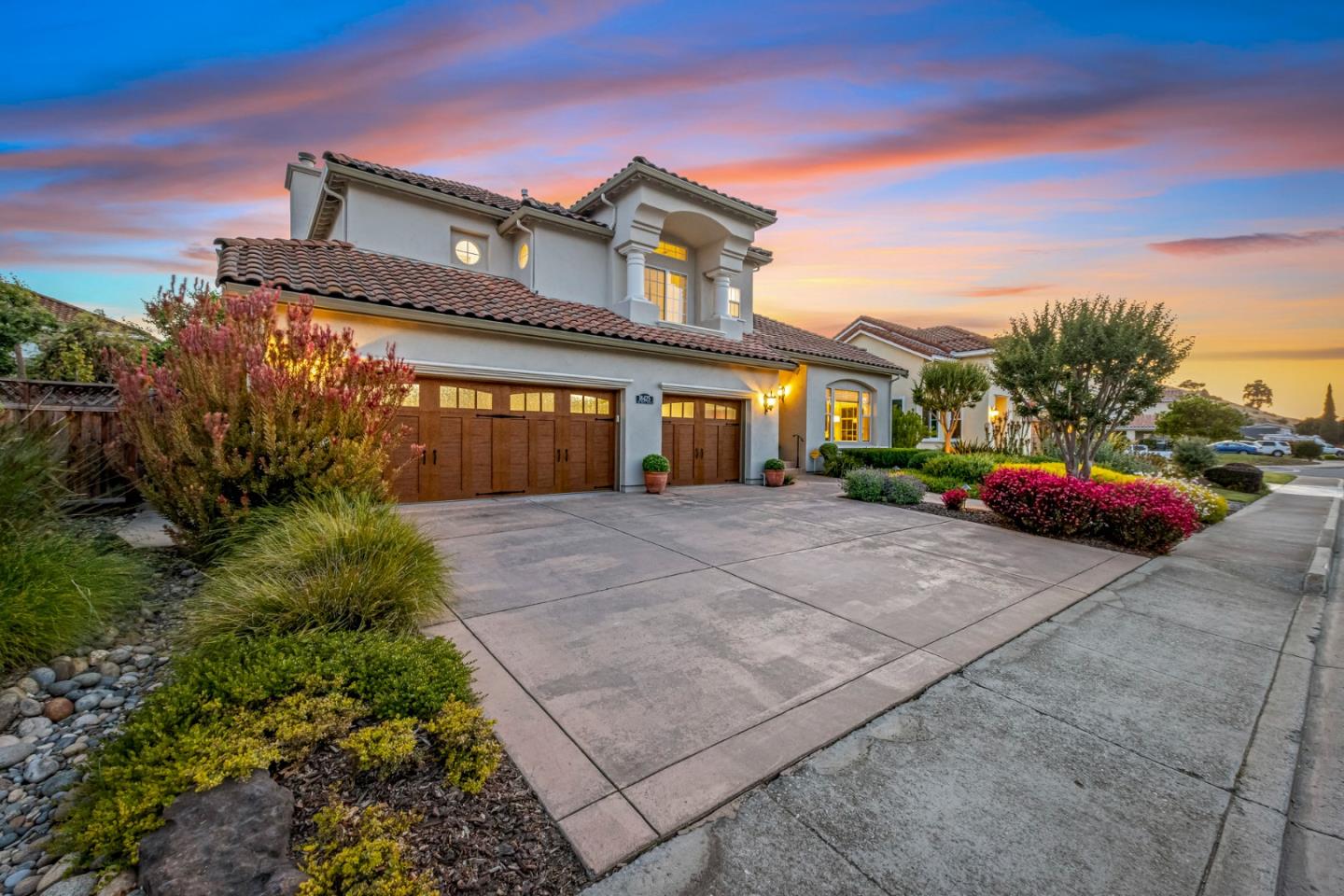 Two-story stucco home with wooden garage doors and landscaped front yard at sunset.