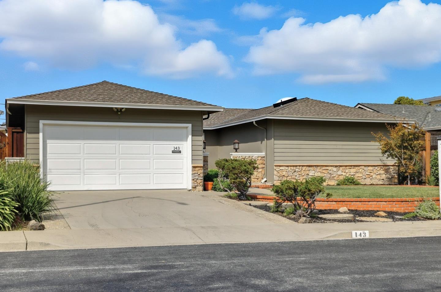 Single-story gray house with a white double garage, stone veneer, and landscaped front yard.