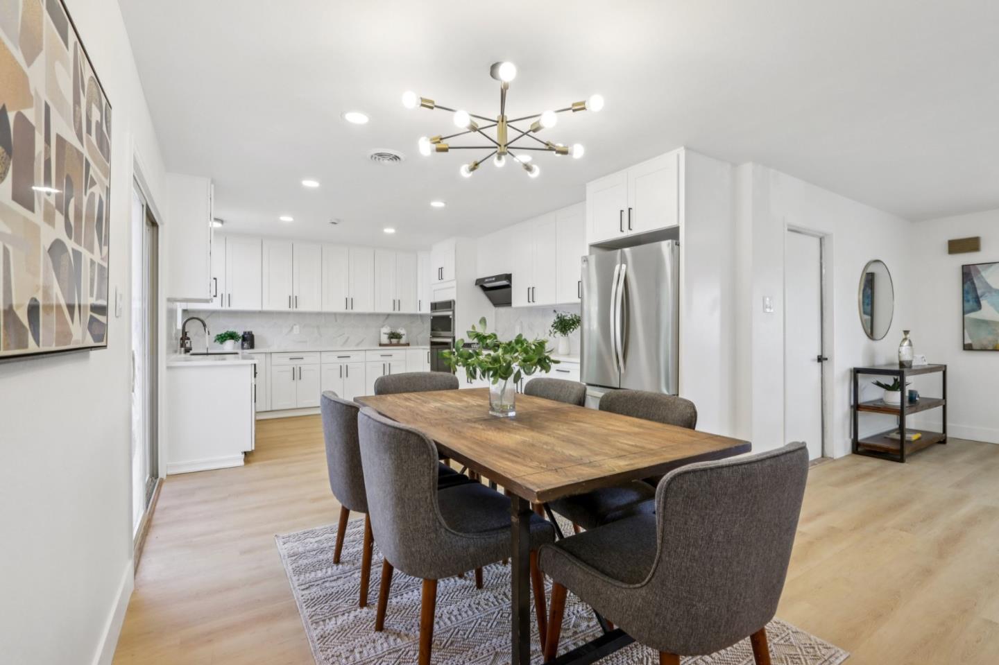Open-plan kitchen and dining area with white cabinets, stainless appliances, and a large wooden table.