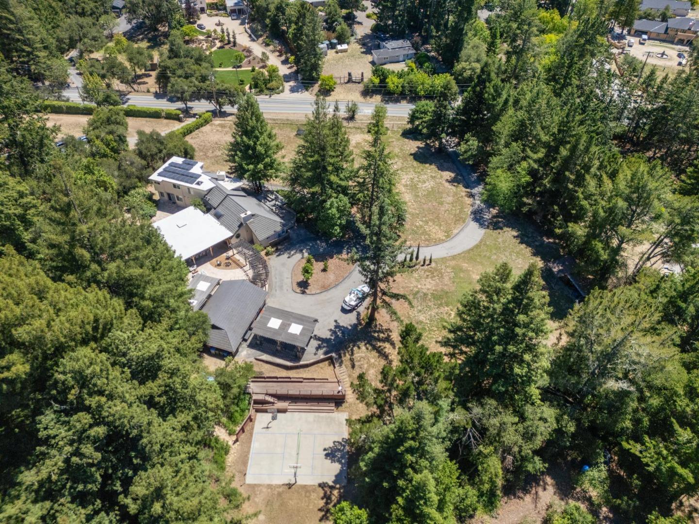 Aerial view of a wooded home with rooftop solar panels, a curved driveway, and an outdoor court.