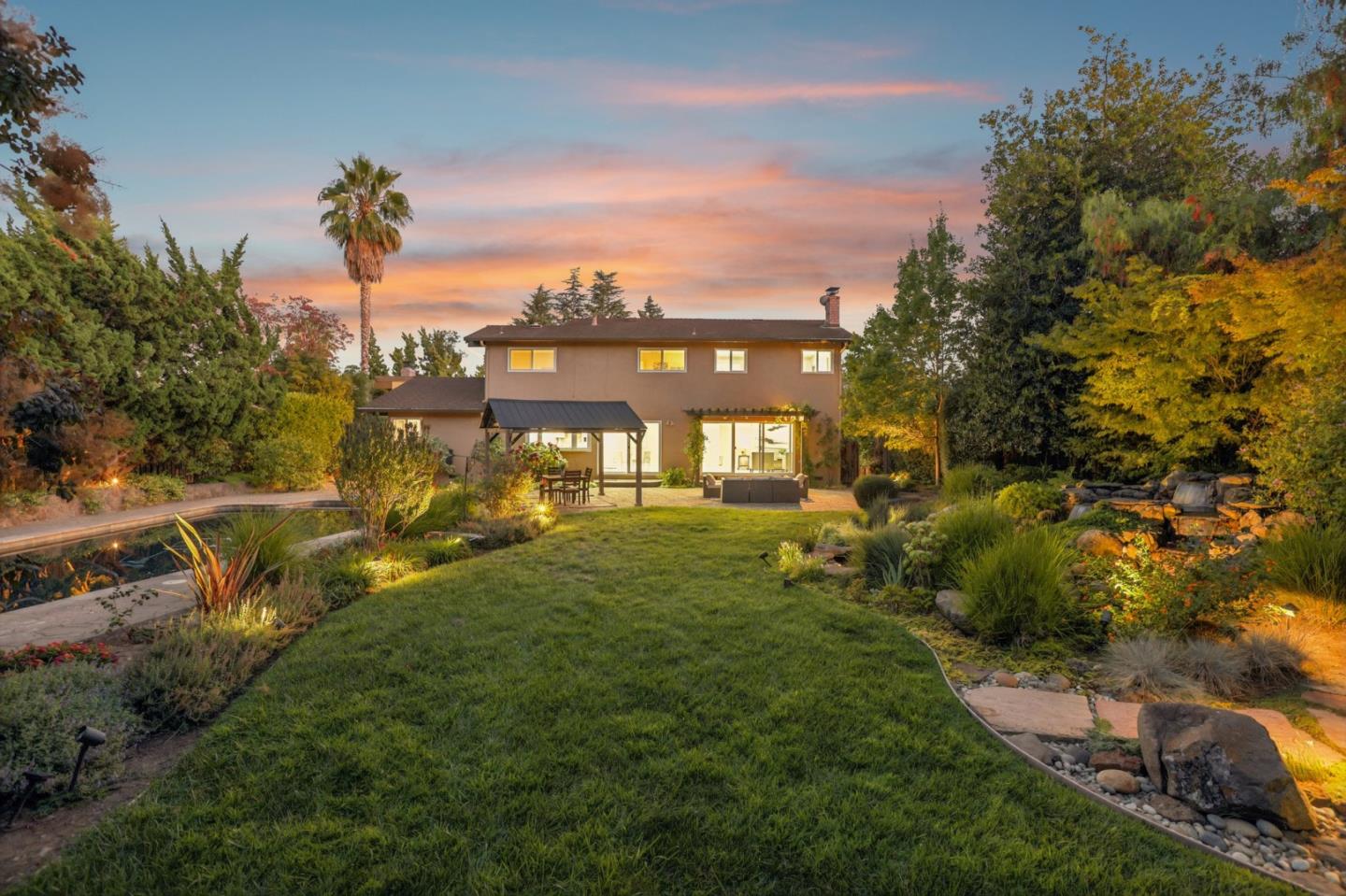 Two-story home behind a landscaped lawn, with outdoor seating and a narrow pool beneath a pink dusk sky.