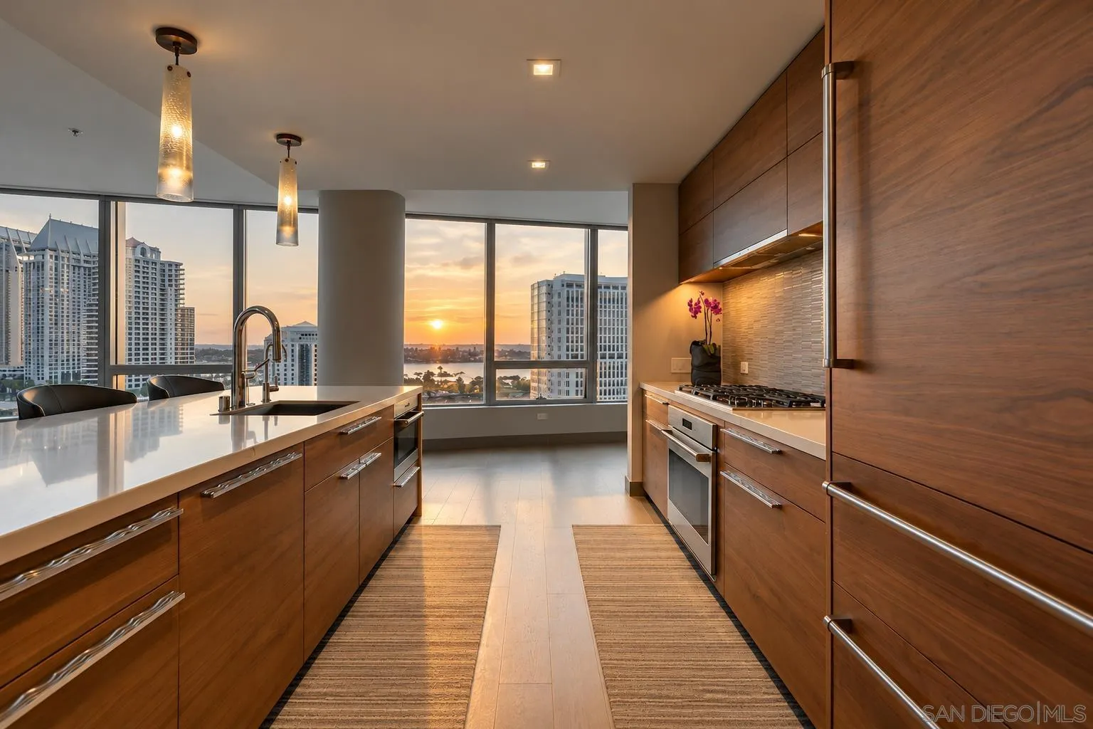 Modern wood-paneled kitchen with a white island and downtown and bay views at sunset.