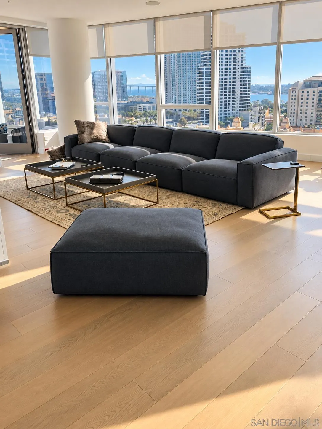 Living room with a charcoal sectional and floor-to-ceiling windows overlooking downtown San Diego and the bay.