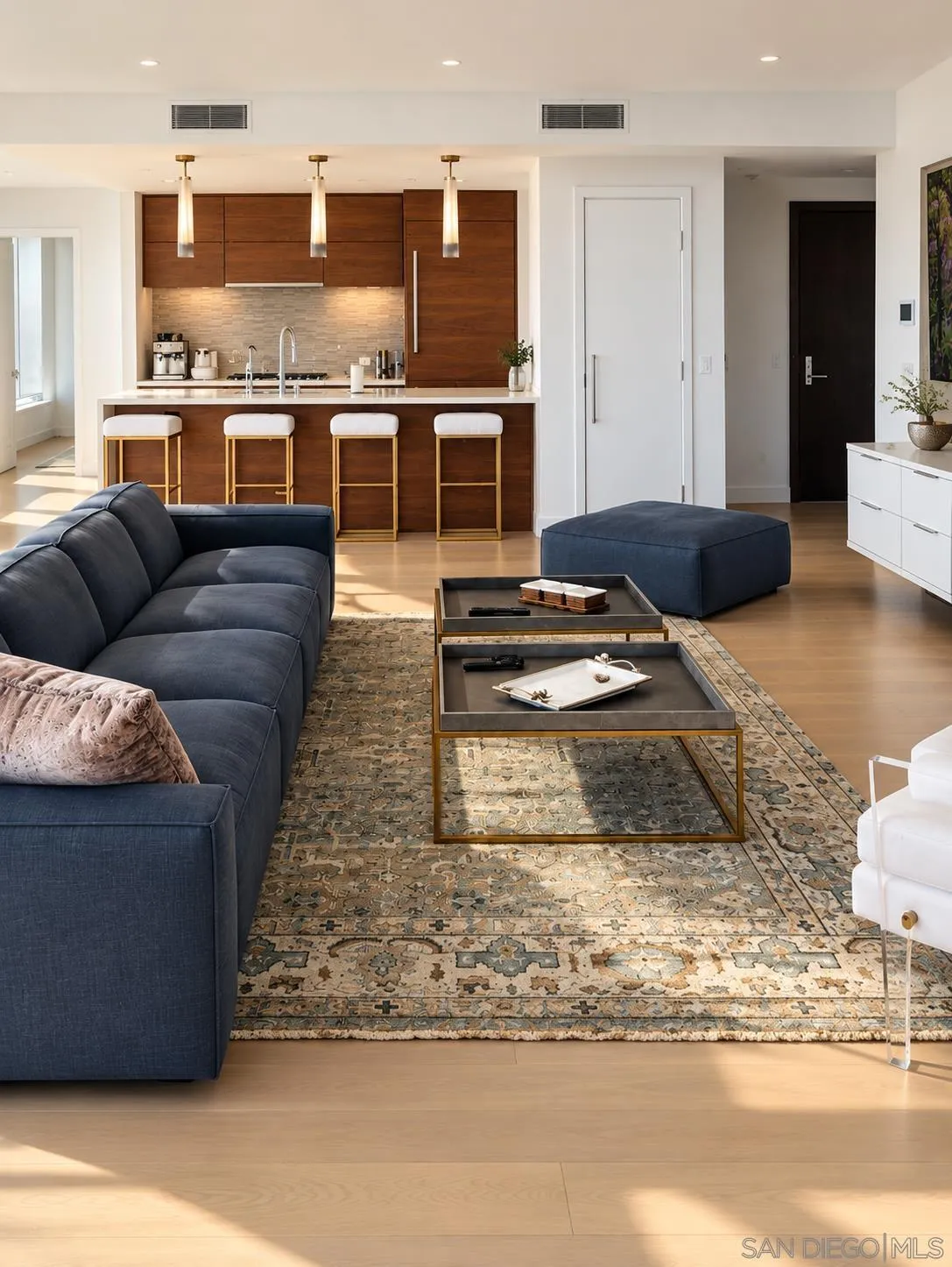 Living room with dark blue seating, a patterned rug, and an open kitchen with wood cabinetry.