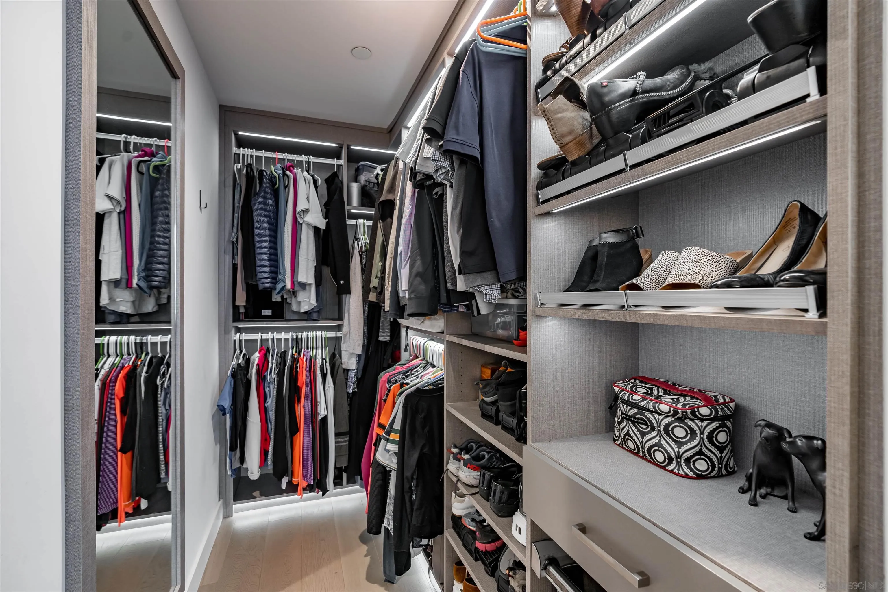 Walk-in closet with built-in shelving, hanging clothes, and rows of shoes.