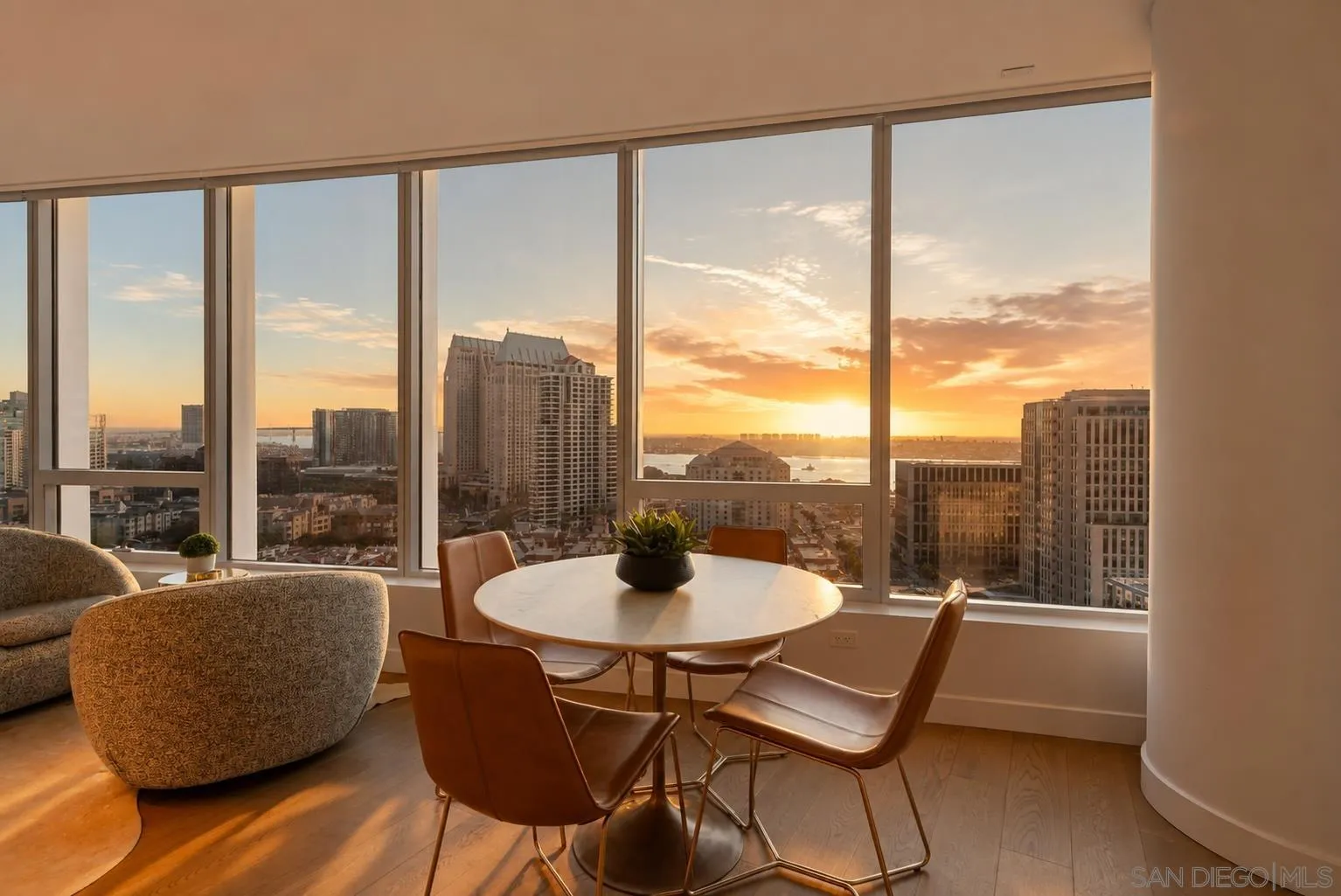Condo dining area with floor-to-ceiling windows overlooking downtown San Diego and the bay at sunset.