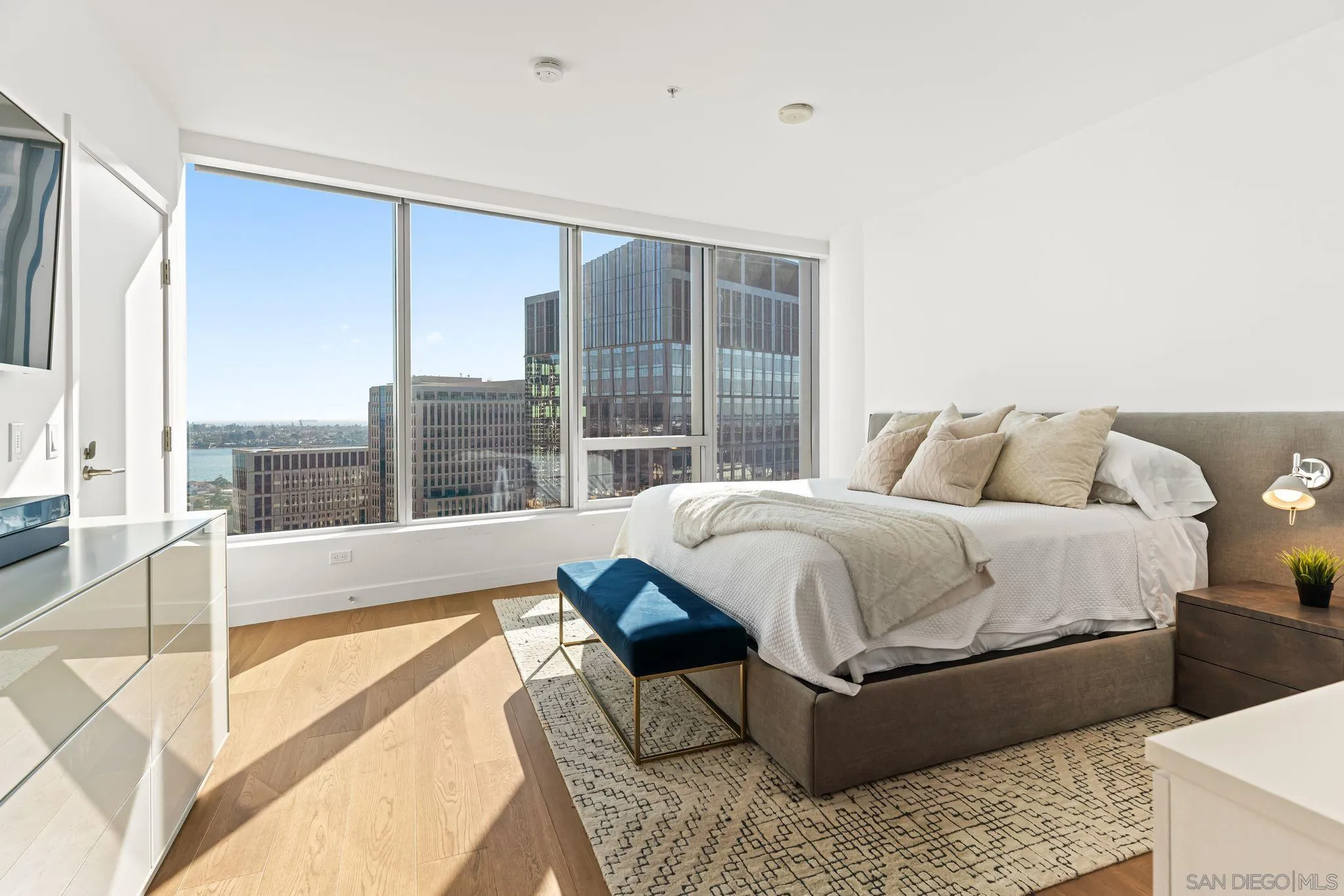 Furnished high-rise bedroom with floor-to-ceiling windows overlooking downtown buildings and water.