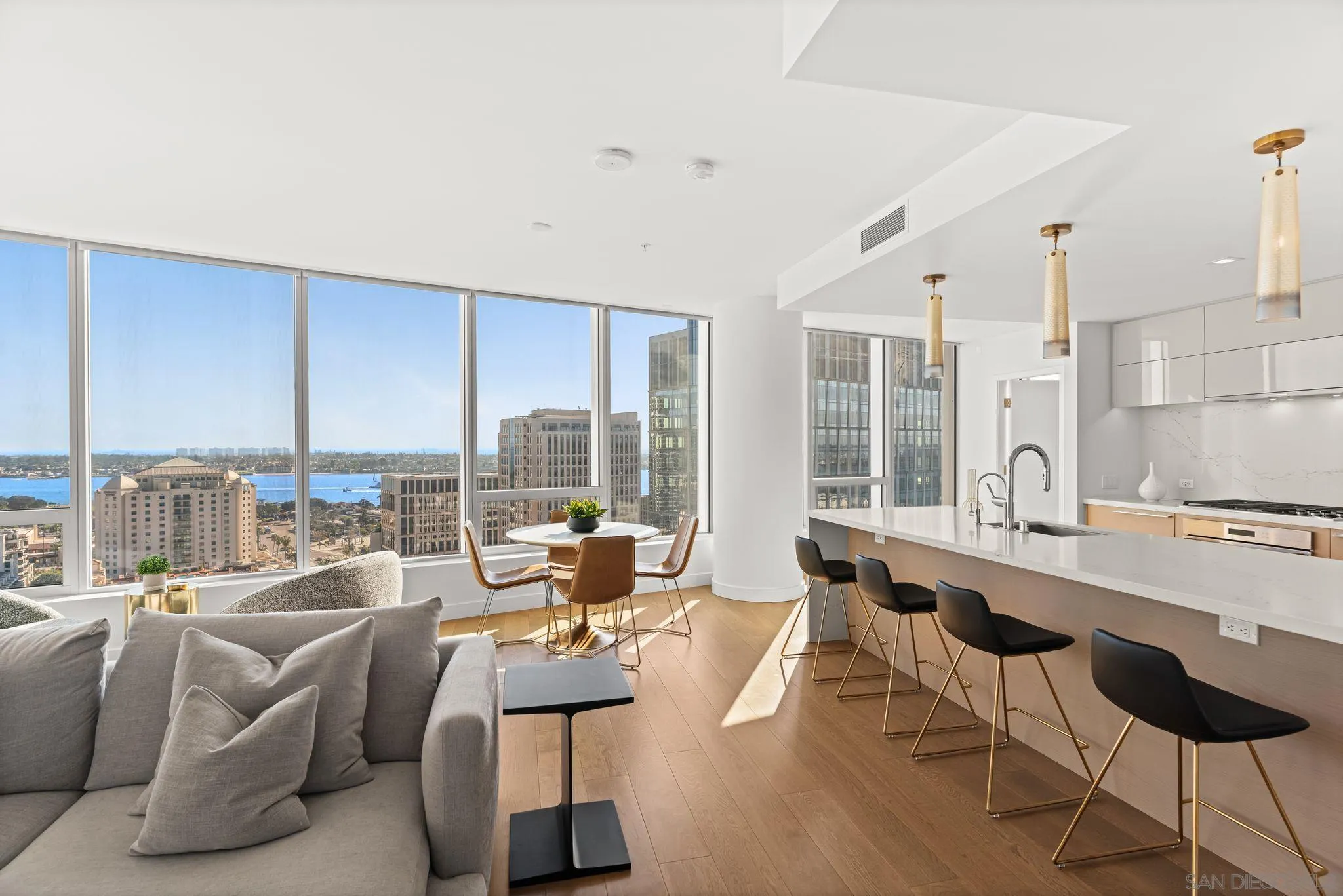Open-plan condo living room and kitchen with floor-to-ceiling windows overlooking San Diego Bay and downtown.