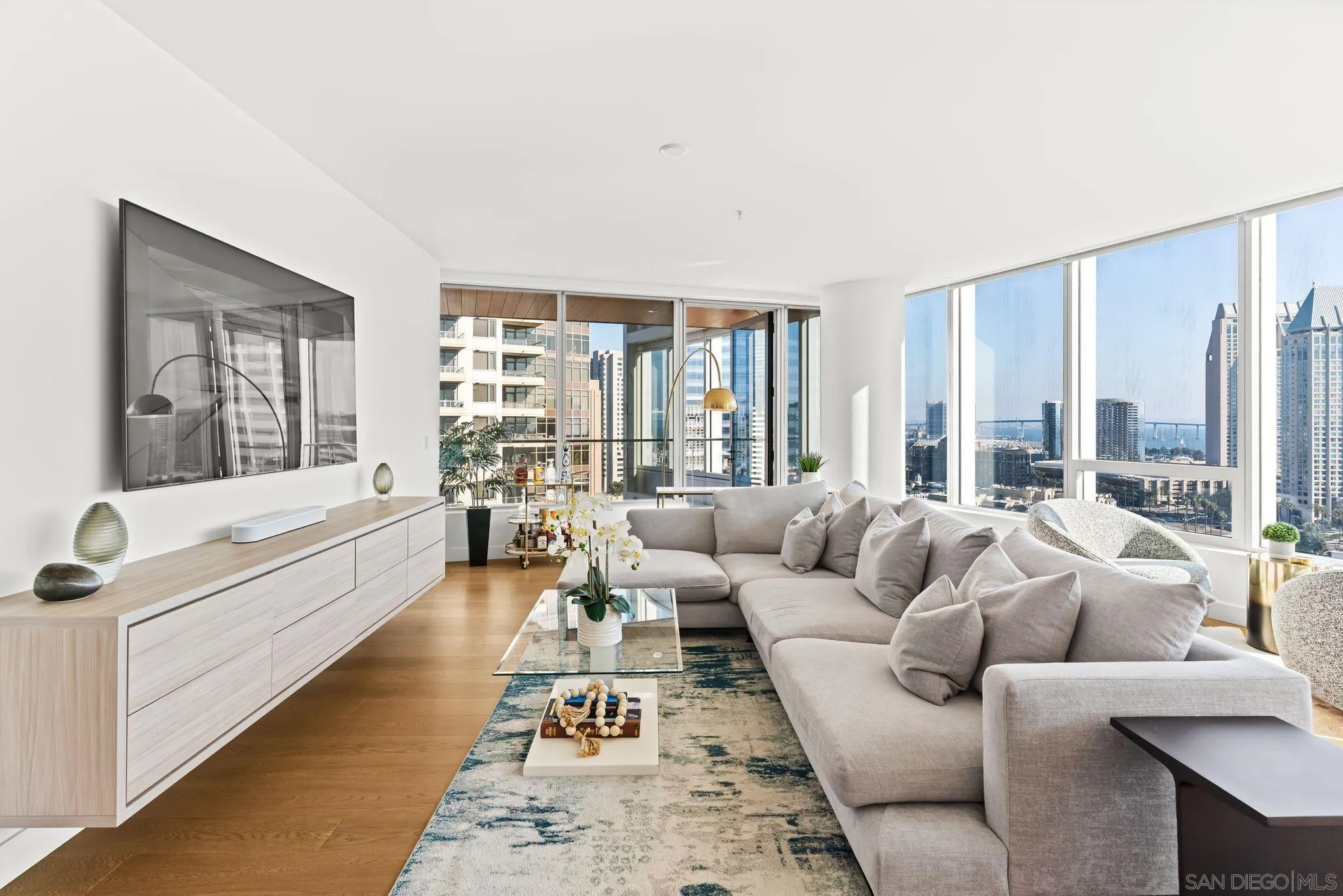 Furnished condo living room with floor-to-ceiling windows overlooking the San Diego skyline and bay.