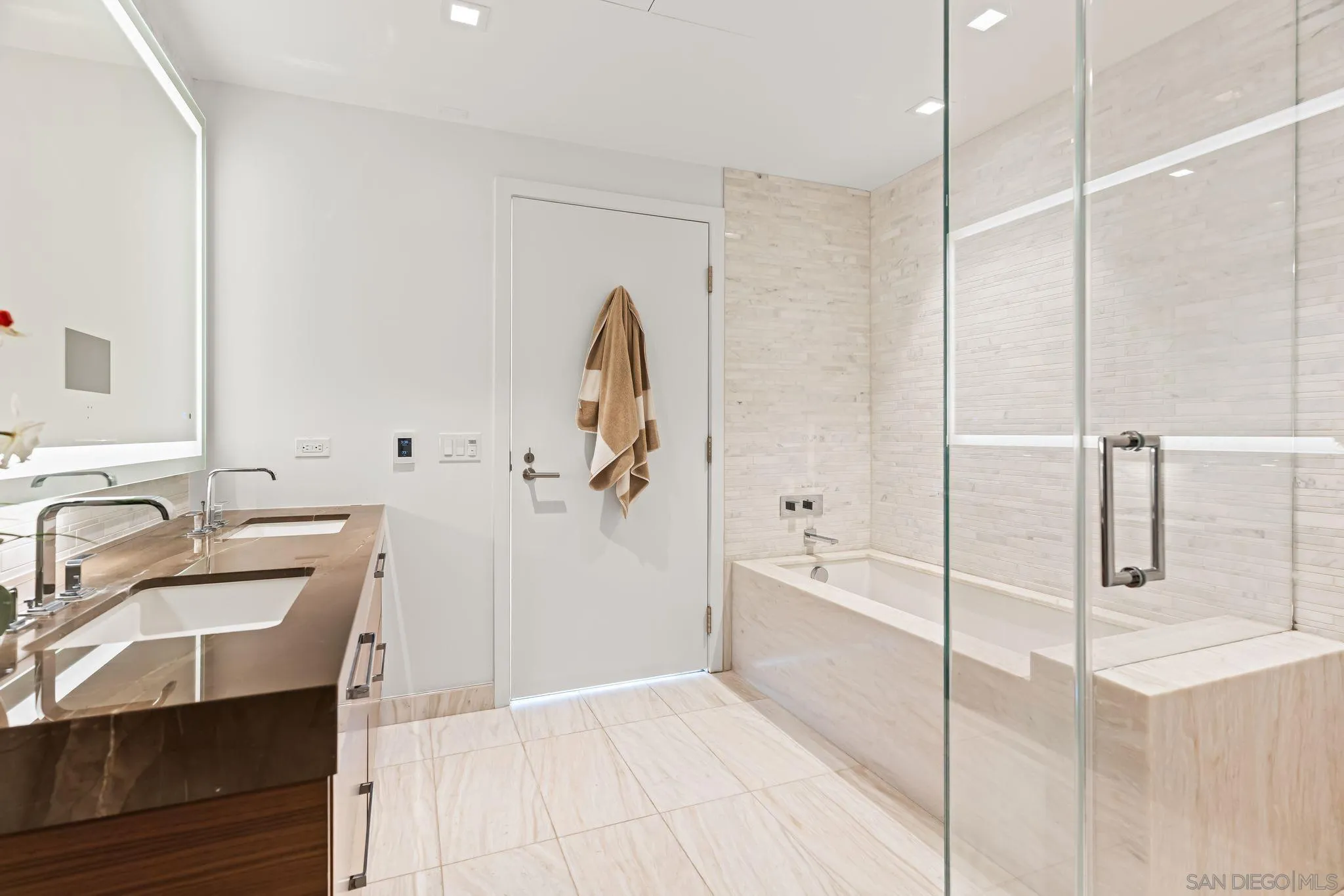 Modern bathroom with a double vanity and a soaking tub behind a glass shower enclosure.