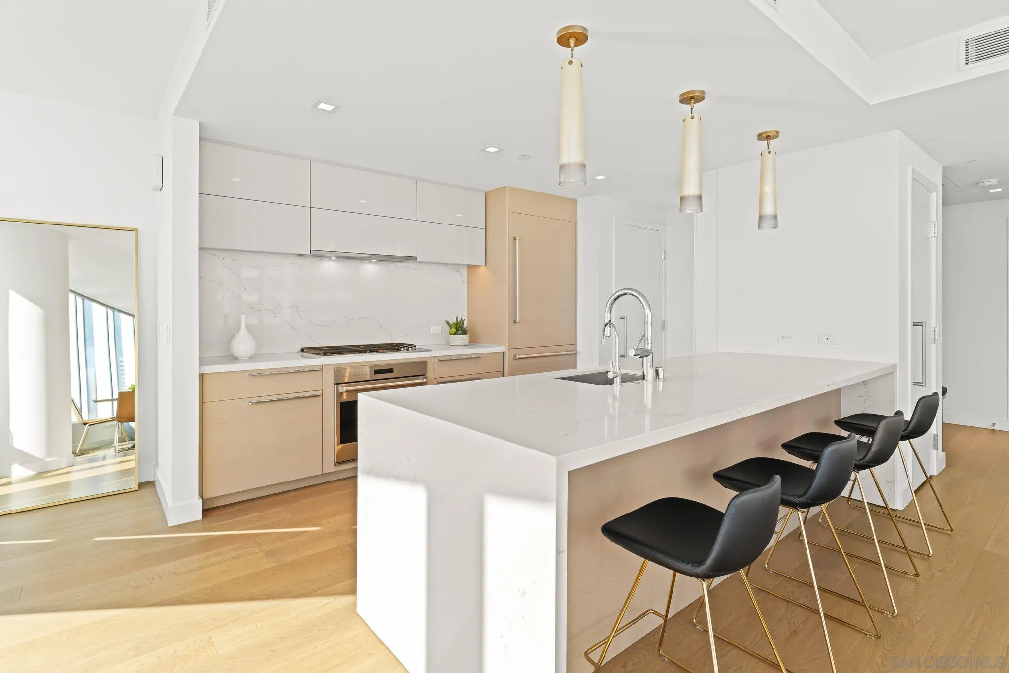 Modern condo kitchen with a large waterfall island, light wood cabinetry, and black bar stools.
