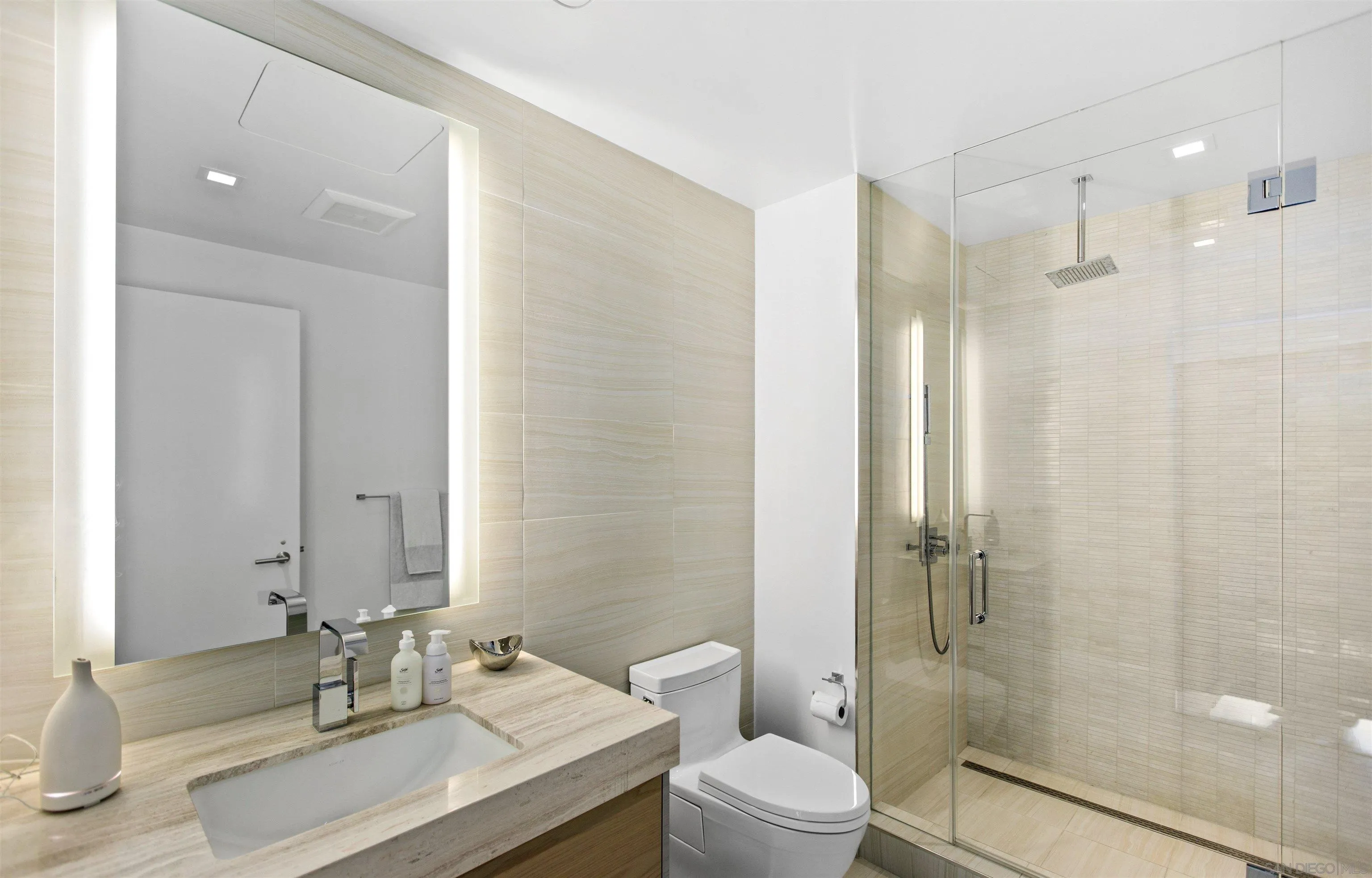 Modern bathroom with a stone vanity, illuminated mirror, and glass-enclosed walk-in shower.