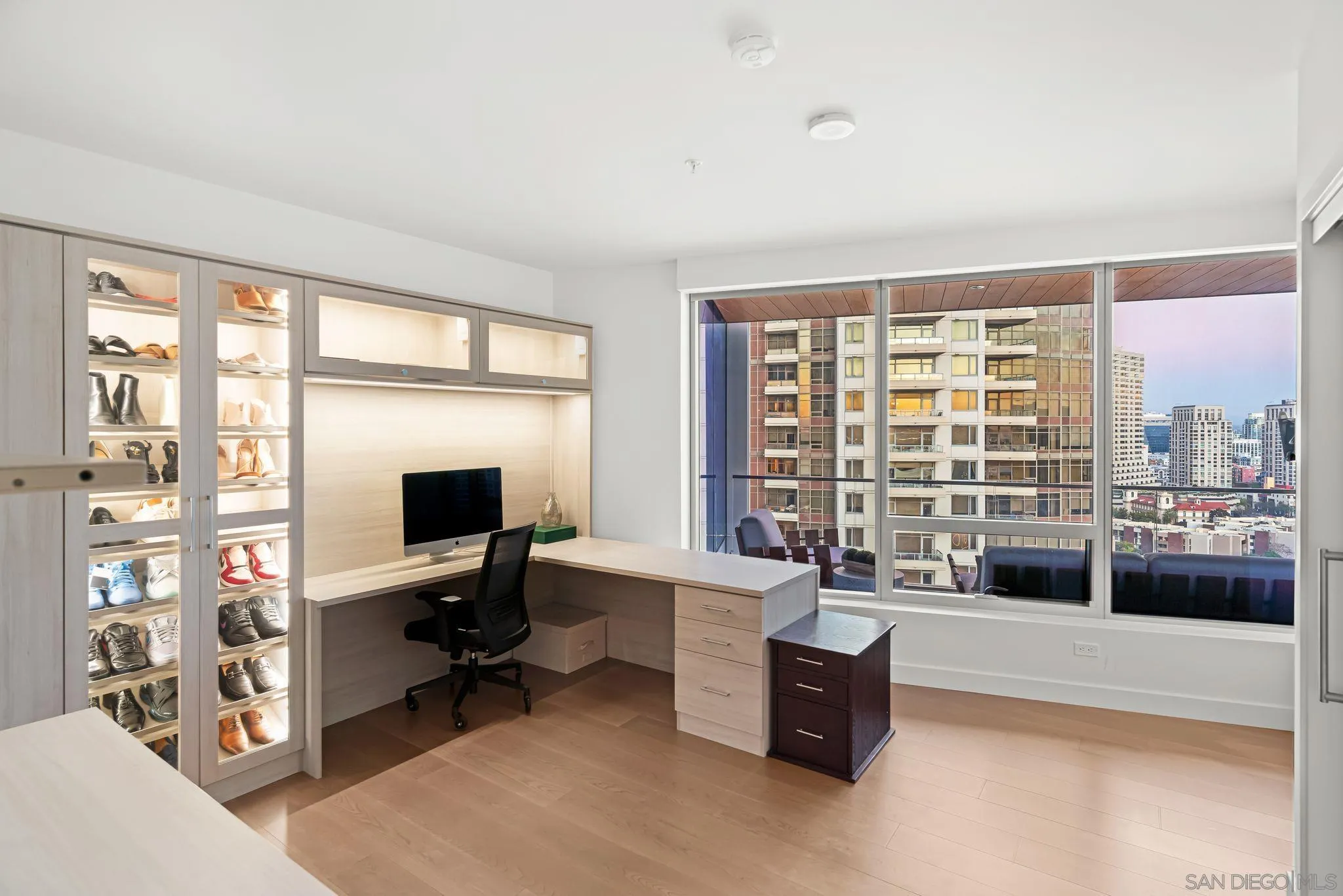 Furnished condo office with illuminated shoe cabinets and floor-to-ceiling windows overlooking the city.