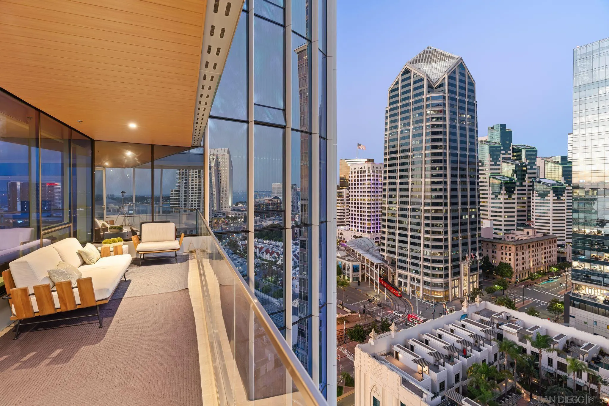 Furnished condo balcony with white seating overlooking the downtown San Diego skyline at dusk.