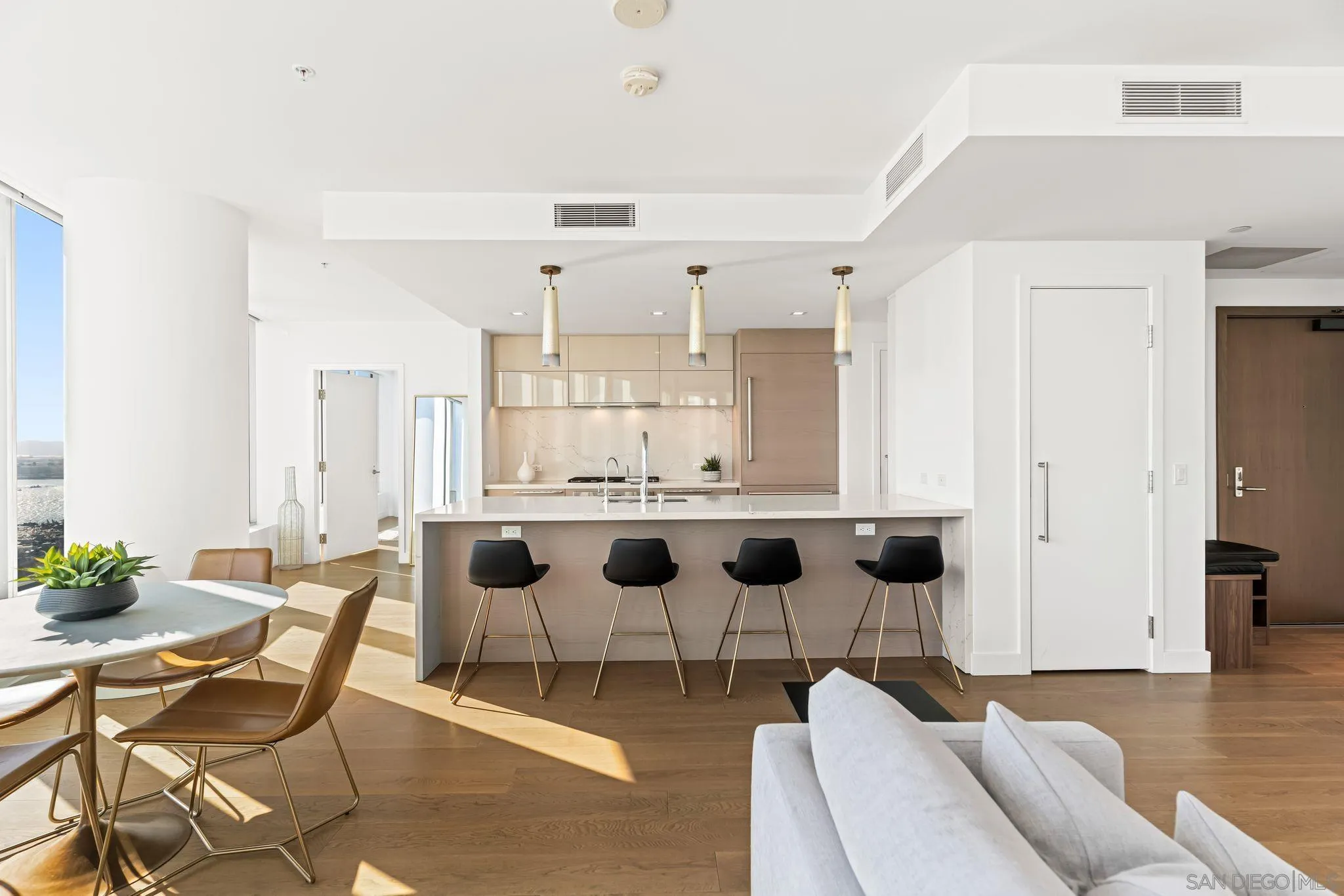 Open-plan kitchen with marble island, four black stools, and tall windows overlooking the water.