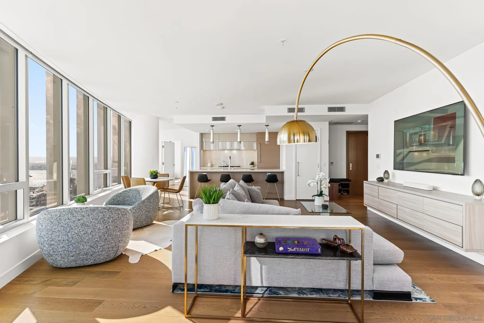 Open-plan condo living room with floor-to-ceiling windows, gray seating, and a modern kitchen.