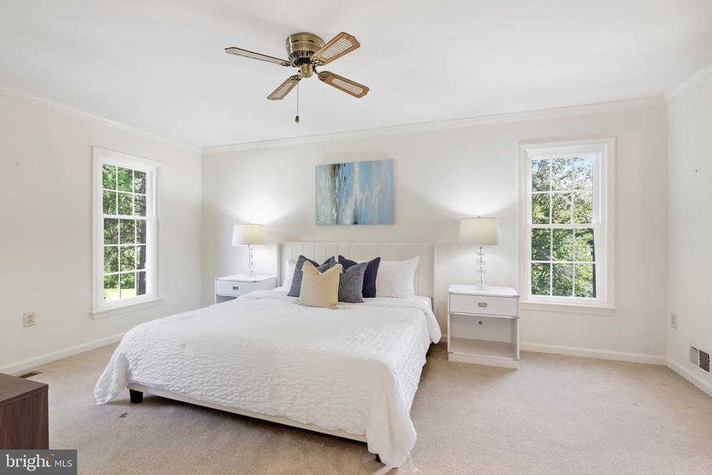 Staged bedroom with a white bed between two windows and a ceiling fan.