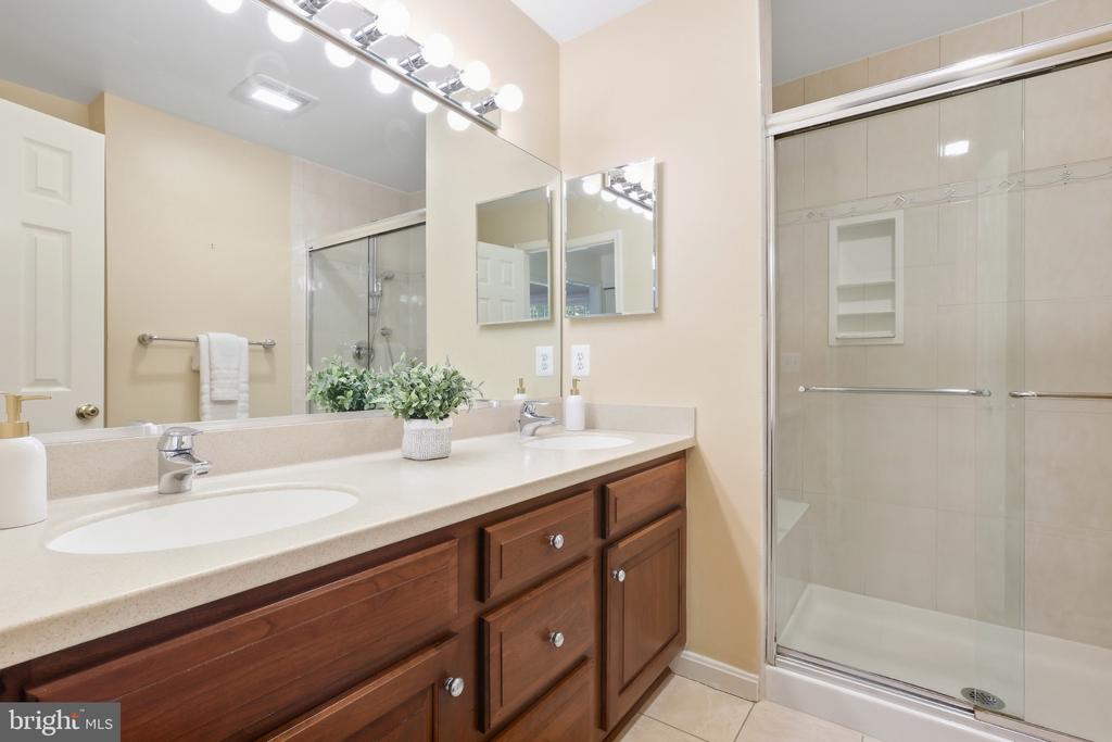 Bathroom with a wood double vanity, large mirrors, and a glass-enclosed shower.