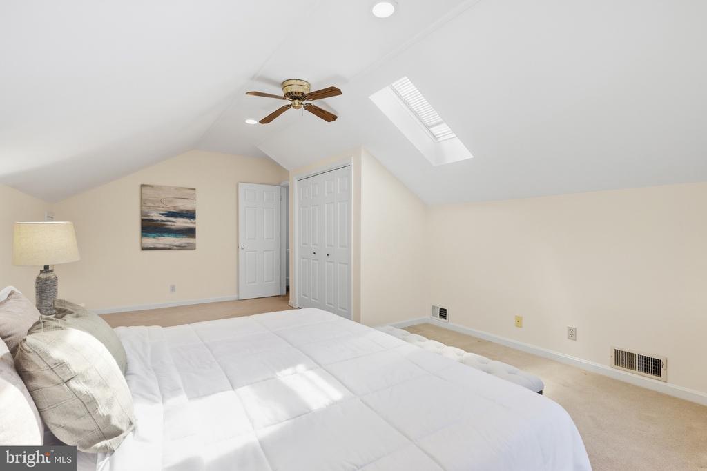 Furnished bedroom with a large white bed, sloped ceiling, ceiling fan, and skylight.