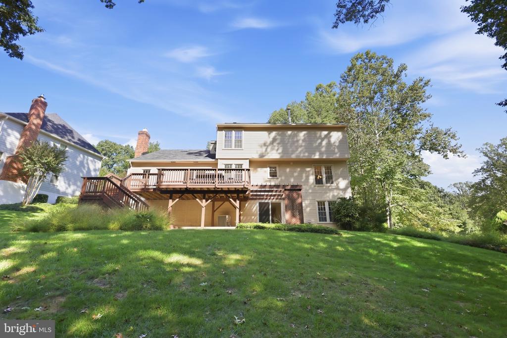 Rear of a two-story house with a raised deck overlooking a broad lawn.
