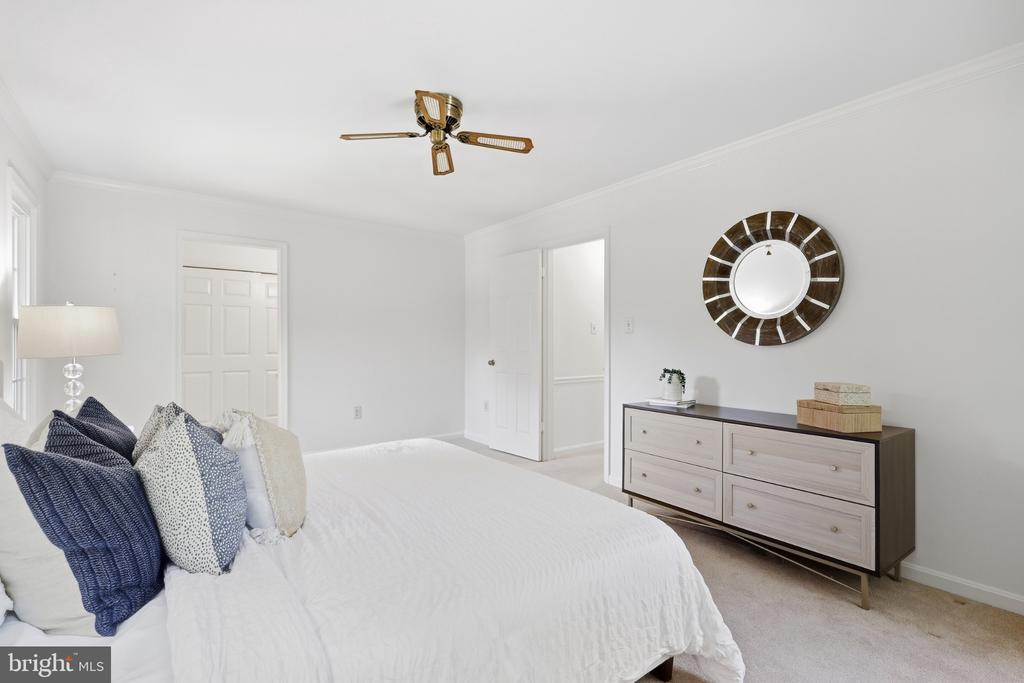Bedroom with a white bed, navy pillows, light dresser, round mirror, and ceiling fan.