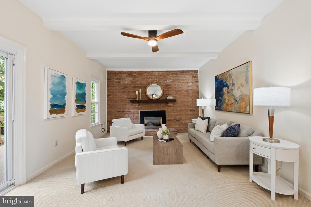 Staged living room with a brick fireplace, neutral seating, abstract art, and a ceiling fan.
